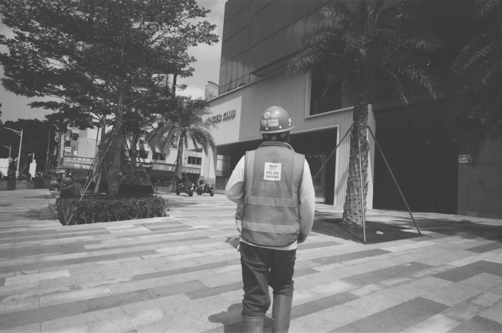 Construction worker in safety vest walks on patterned sidewalk.